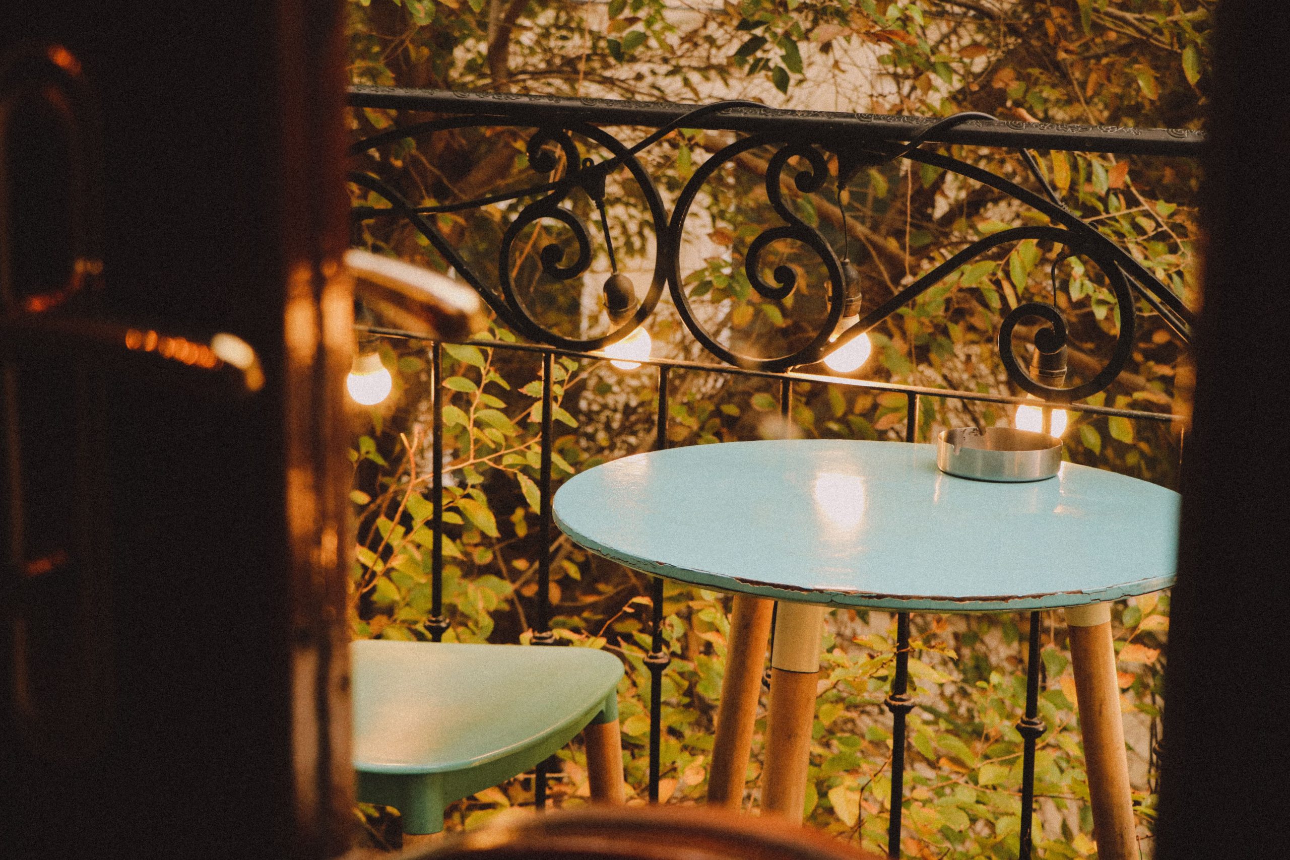 Small balcony with a blue table, chair, and warm lights creating a serene evening vibe